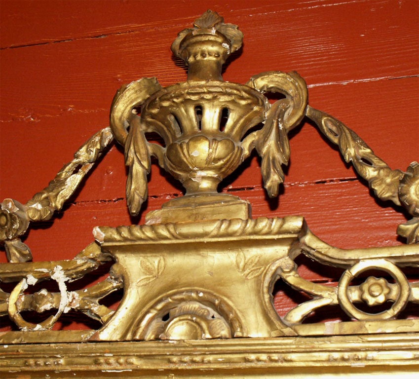 The mirror is crowned with a carved urn and garland.  The old mirror is bordered by eglomise strip of green and black glass in a faux marble pattern and flanked on both sides by a gilt molding