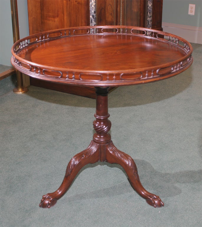 The tilt-top surmounted by a pierced brass-line inlaid gallery; raised on a turned, spiral-fluted columnar support on three foliate-carved downswept legs ending in ball and claw feet.