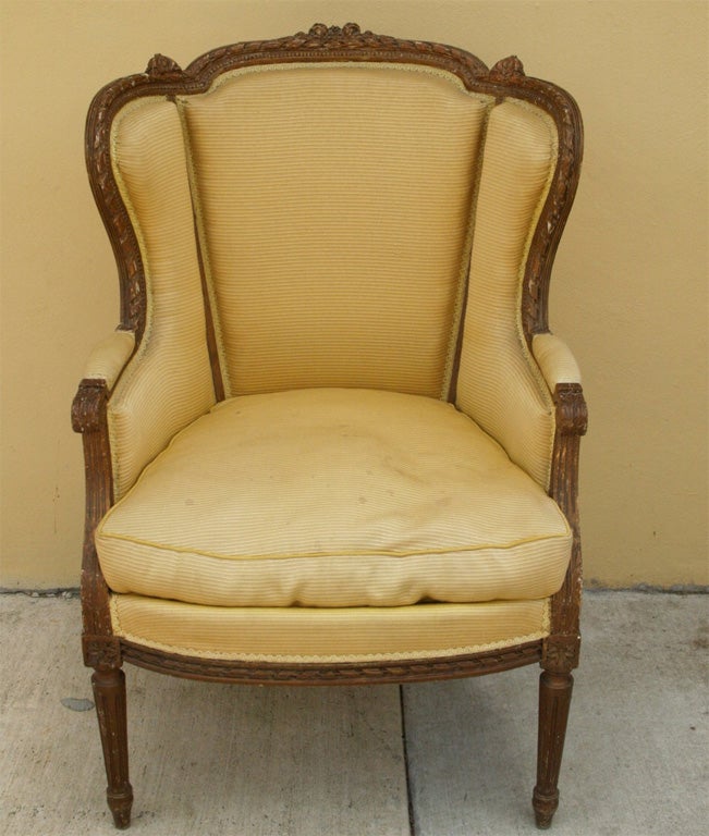 Louis XVI style bergere with upholstered rounded back, traditional Louis XVI style decorative carving and fluted, tapered leg. The gold, ribbed textured, ottoman cloth upholstery shows age and some fading.  The height of the back is 40