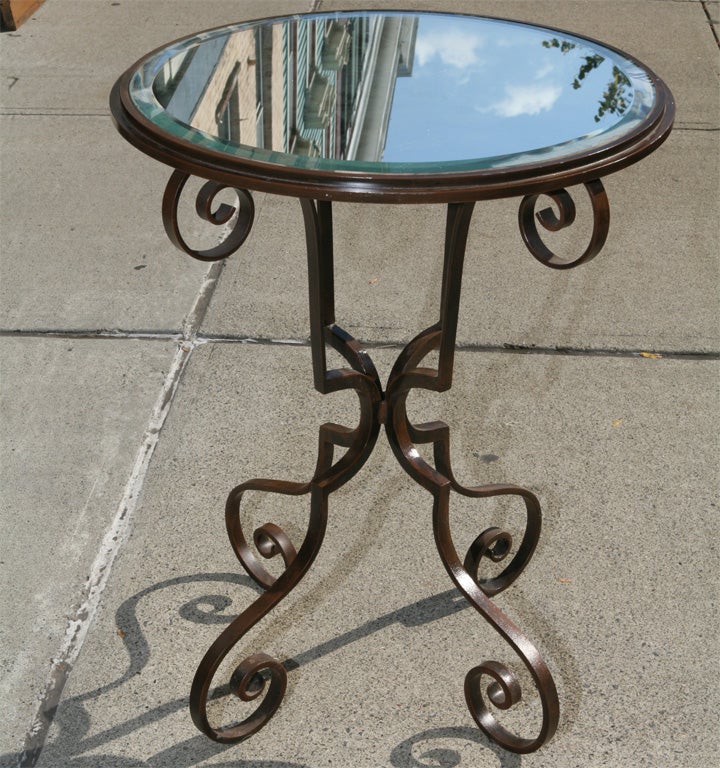 A very nice wrought iron bistro style table perfect to use as a side table or hall center table in a small space. The iron base has a painted finish which appears in different light to be a brown then a brown green color. The distressed mirrored top