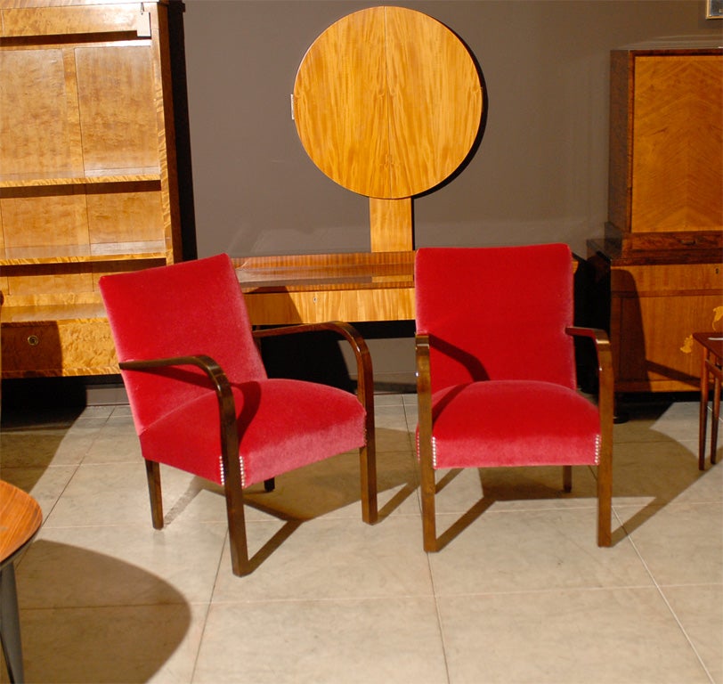 Pair of Art Deco influenced streamlined Moderne chairs, crafted of dark flame birch, completely restored and newly upholstered in luxurious cherry red mohair fabric trimmed with pewter finish nail head tacks.  Hardwood frames and eight-way hand-tied