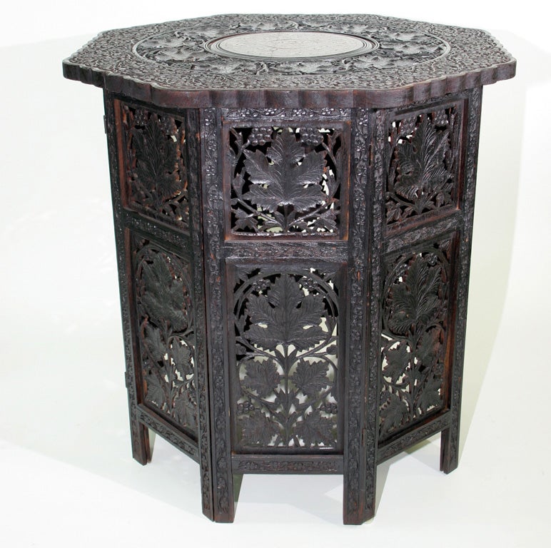 A carved octagonal table, the top consisting of tripartite design of floral, leaf and inlaid brass resting on pierced foliate folding base.