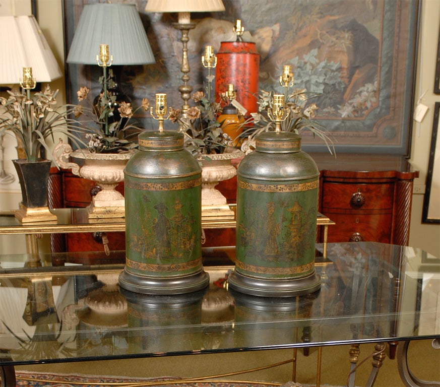 A pair of semi-cylinder English shop tole tea canisters with original black and gold decoration in the chinoisserie style on a green ground now mounted and newly wired as lamps with custom wooden bases.