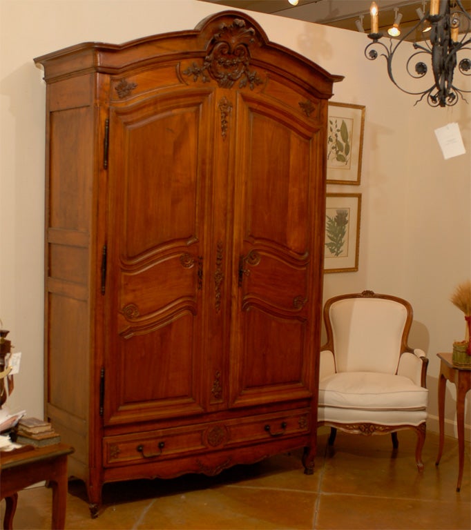 A French Louis XV style cherrywood armoire from the 19th century, with carved crest, two doors and four drawers. This exquisite French armoire features a molded bonnet shaped pediment, carved in its center with an acanthus leaf, C-scrolls and floral