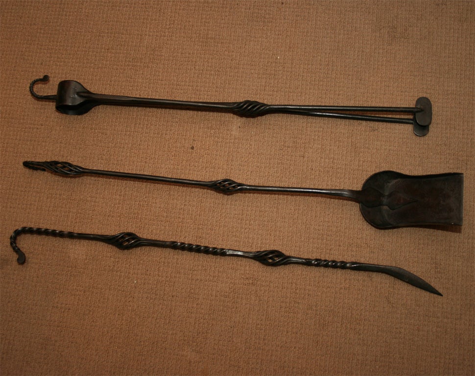 A set of three English Arts and Crafts firetools comprising shovel, poker and tongs, the shovel with decorative shaped support, and all with forged iron shafts and sprung twists ending in hooks for hanging the tools.