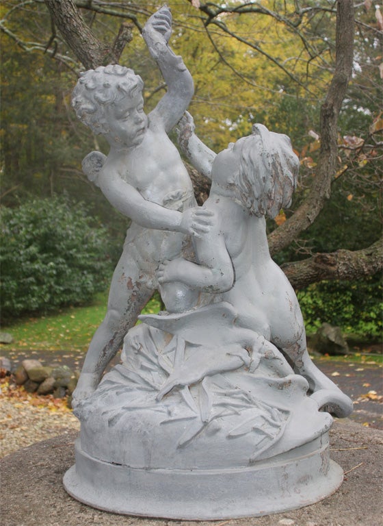 In lead & zinc, this signed fountain depicts, the triton & the cherub playfully fighting over a fish