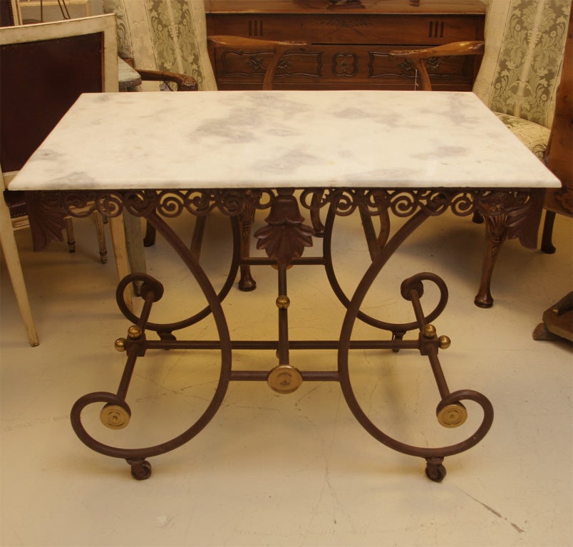 White marble top with black painted iron base ..Pierced, scrolled and
foliate apron above four scrolled legs on castors.Stretcher joins legs' 
Brass accents on base