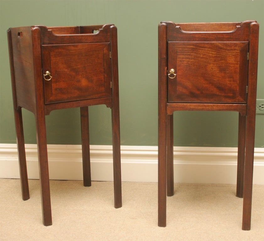 A fine pair of mahogany end tables with very good color, each having a wood gallery with pierced handles, the fronts with a single cupboard door and original brass handles.