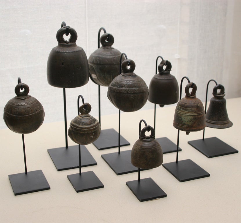 A collection of bronze bells in various sizes and shapes, on stands, each with unique patterns.  Bells range in size from 2 1/2