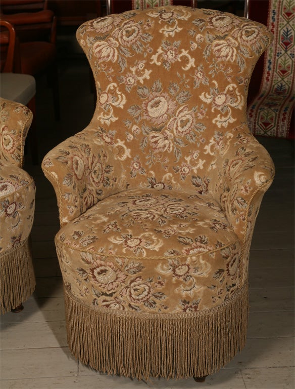 Pair of late Victorian parlor chairs, his and hers, covered in chenille fabric with generous fringe at the bottom