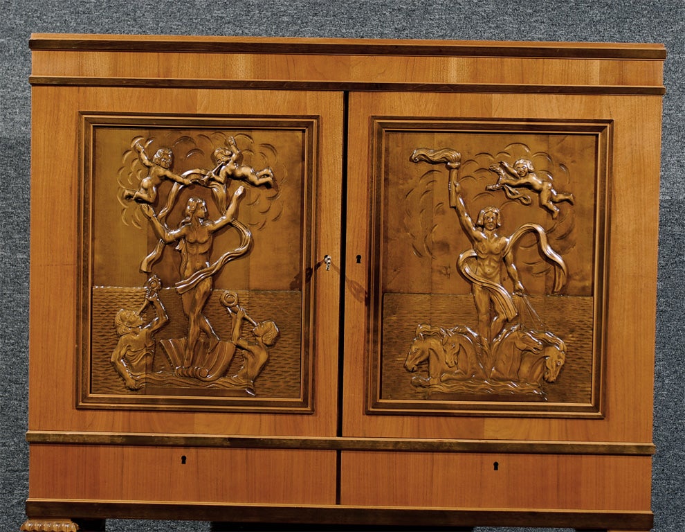Intricately hand-carved cabinet of various woods including walnut, mahogany and dark flame birch. Carved inset doors feature mythological figures. Features two locked drawers with key and three adjustable interior shelves. Made by Svenska