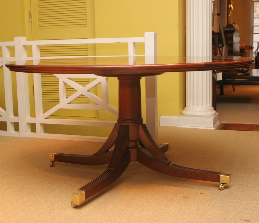 An exceptional hand made and custom designed circular mahogany dining table featuring antique mahogany veneers, on a custom quadruped pedestal support with brass caps and castors, with five semi-circular leaves which expand the table to an 80