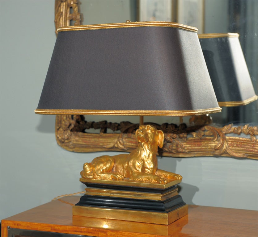 Each in the form of a recumbent Brittany Spaniel; mounted on later rectangular plinths of gold and black metal; now museum wired as lamps; contemporary drum rectangle shades in black silk with gold trim and gold foil lining.