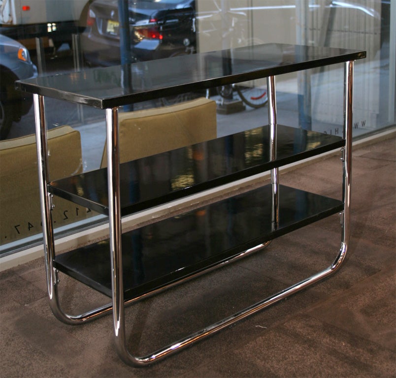 Machine Age style end tables with<br />
tubular chromed legs, three<br />
black lacquered tiers, and vitrolite<br />
tops.