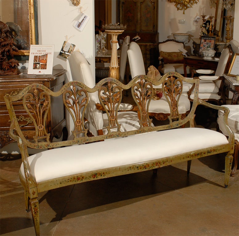 A Venetian 18th century painted and gilt wood sofa with new upholstery. This rare Italian sofa features a pierced back, surmounted by a sinuous rail, adorned with delicate painted floral motifs. This back is decorated with five pierced splats, each