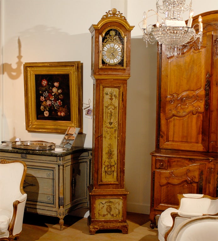 A French parcel gilt and red painted longcase grandfather clock from the 19th century, with carved crest and classical décor. Born in France during the early years of the 19th century, this long case clock features a rectangular head, adorned with a