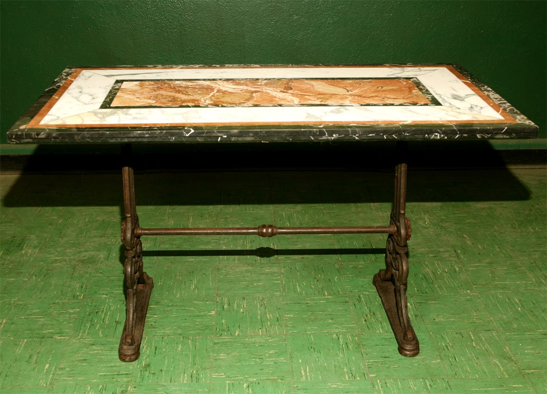 This classically inspired cast iron table has an Italian specimen marble top in three colors. The iron base incorporates acanthus leaf casting and large boss rossets at the ends of the cross stretcher. The surface of the table has its original