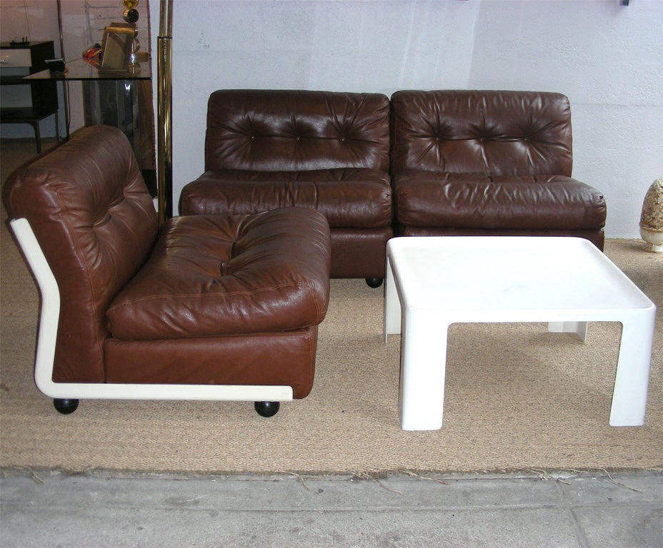 1970s living-room suite by Mario Bellini, with label underneath, composed of one armchair, one two-seater sofa and a coffee table. Outer white resin shell and brown leather upholstery. Table height 36 cm., length and depth 70 cm. Armchair height