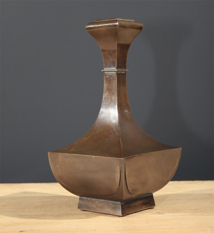 A finely crafted Japanese bronze vase of crisp, geometric design. The vase loosely based on the Chinese garlic bulb vase form. The vase with square rimmed mouth, narrow neck with decorative band flaring to a sharpened edged hipped body. The vase