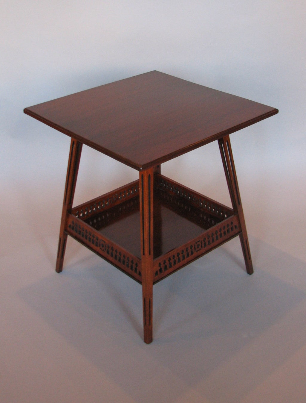 An unusual Liberty's Aesthetic period mahogany side table having one shelf enclosed by a pierced gallery, the legs having pierced cross sections. Bearing an ivorine Liberty & Co. label.