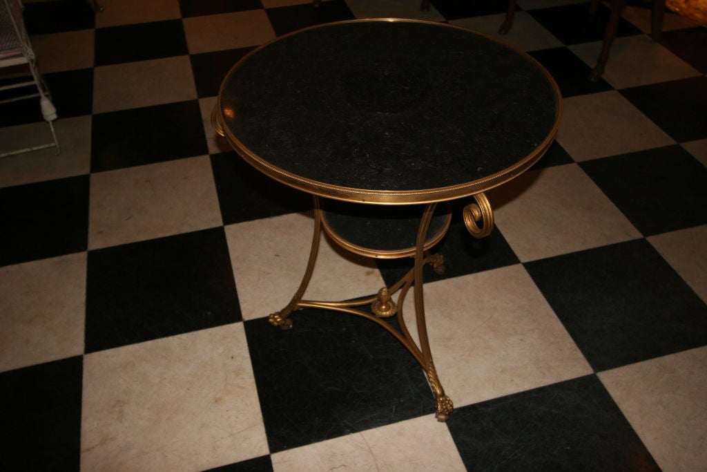 Pair of Empire-Style Gilt-Bronze and Marble-Top Guéridons, each with a circular charcoal marble top joined to a like lower shelf by scrolling supports terminating in an urn-centered stretcher on paw feet to casters,.
