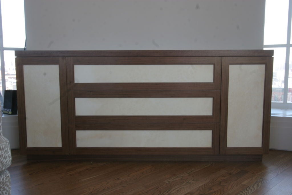 satin walnut surrounds inset panels of Goat skin parchment in this custom motorized, mirror-lined, glass shelved bar.  The side panels are Ash lined with adjustable shelves.  The unit sits on a recessed Walnut base