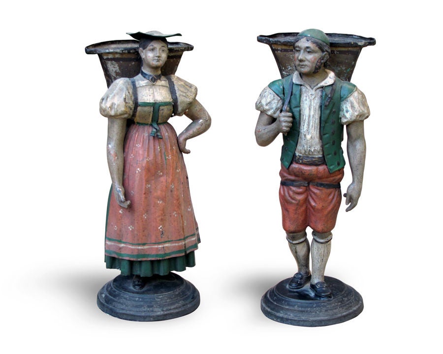 A CHARMING COMPANION PAIR OF GERMAN PAINTED TOLE STANDING FIGURAL BOUQUETIERS OF TYROLEAN HARVESTERS.  Each romanticized female and male figure; realized in expressive and delicate detail donned in Tyrolean costume with flaring, vasiform baskets