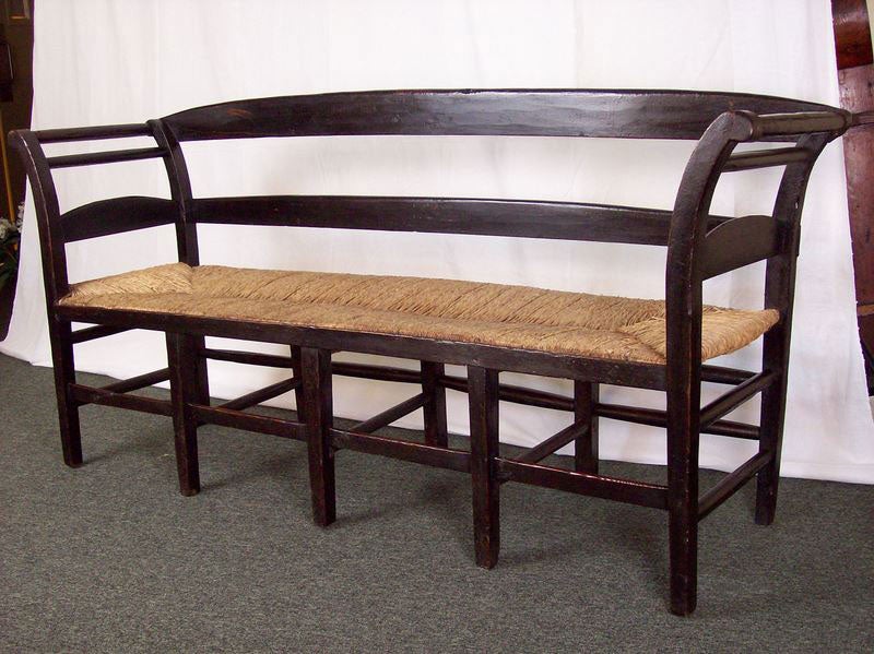 An antique bench from France with a rush seat. Painted black with a tiny bit of red show thru, the curved arms and back of this bench have clean, simple lines. The old rush is in good condition.