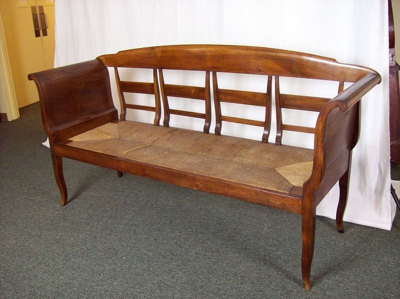 An elegant antique bench from France. The curved arms and legs give this four person bench its distinctive look. The fruit wood has a  beautiful color and patina. There is a pretty inlay on the rails. Old rush is in good condition.