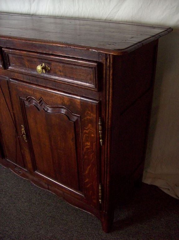 An antique country buffet from France. The oak server is deep in color and rich in patina. Beautifully shaped apron and door panels. One shelf inside for good storage. All the hinges, knobs, and escutcheons are original. Nice shallow depth. Slight