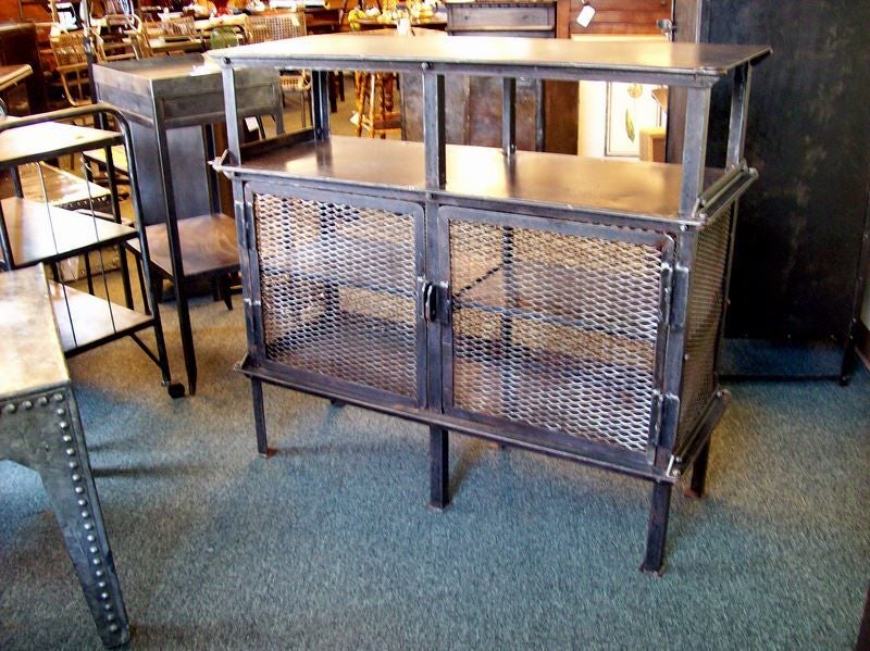 Handsomely detailed industrial steel cabinet,bookcase, or cupboard from France.  Two open shelves above an enclosed storage area make the piece highly functional. Doors held in place by a simple steel bar.  Strongly evocative of a bygone era of
