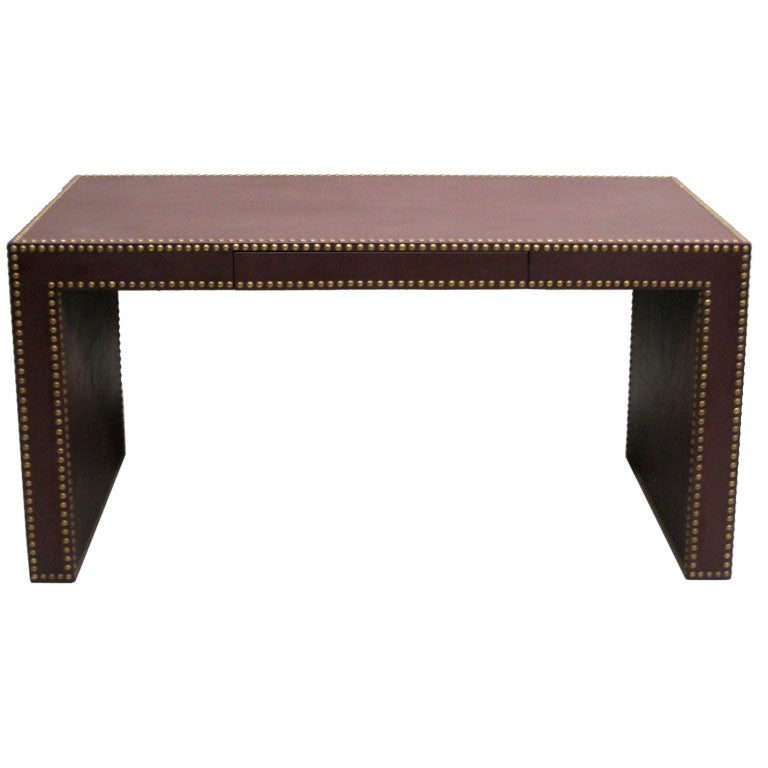 An important midcentury style desk entirely covered in maroon leather and studded with bronze tacks including a leather pencil drawer. A unique, sleek statement blending modern and Minimalist ideas with traditional materials and workmanship. The