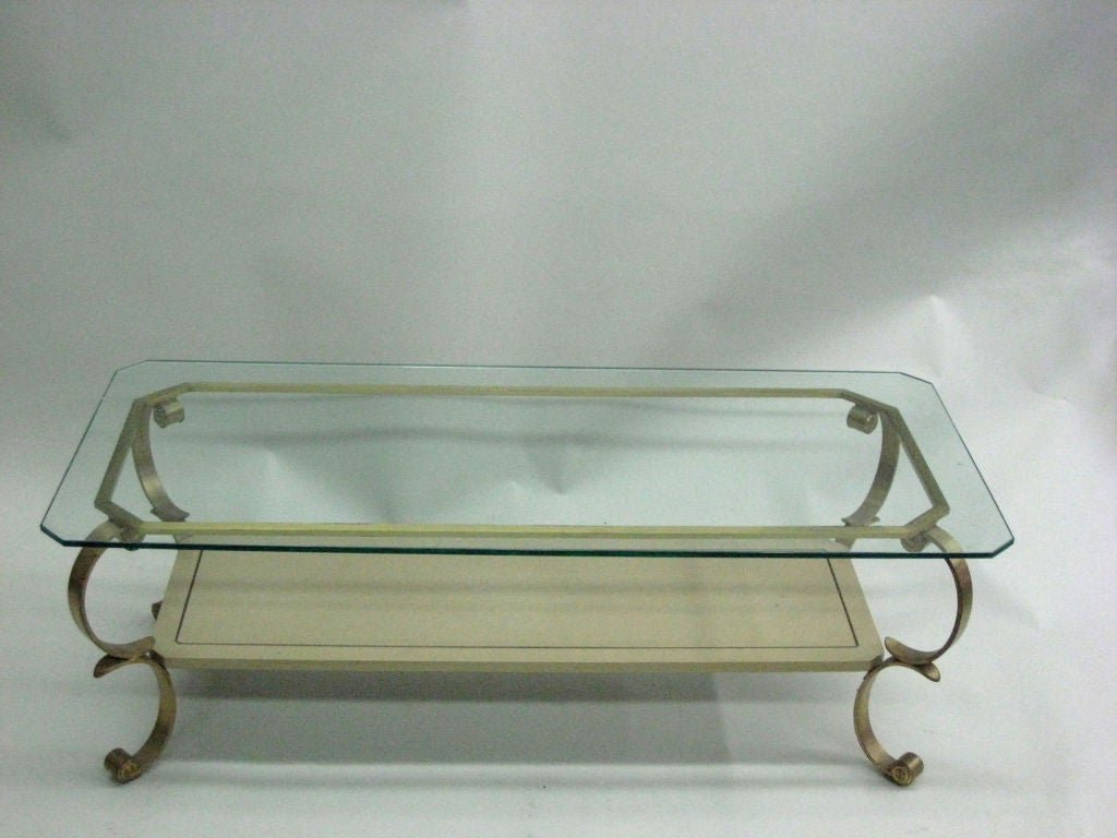 Elegant French Mid-Century Modern neoclassical double level coffee table attributed to Maison Jansen, Paris. The piece is composed of 4 scroll form brass legs supporting a cream lacquered lower panel and a glass top. The lacquer bottom level has an