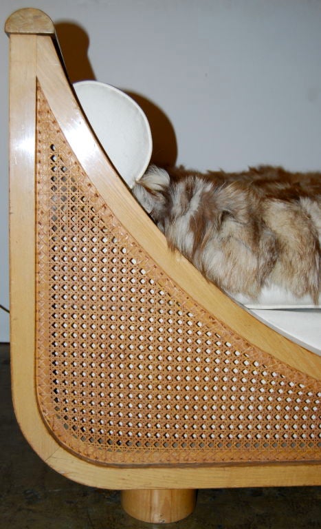 This is a gorgeous daybed designed by the wonderful Jean Royere.  It has a gondola shape with caning throughout the sides and ends. The mattress and bolsters are upholstered in muslin.Fur throw included. Truly lovely and fully