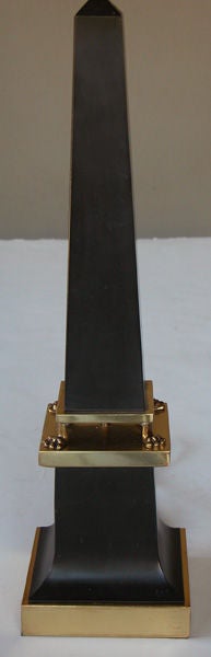 A sleek French 1940's black painted tole obelisk-form lamp with brass mounts; the graduated obelisk-form body raised on 4 brass paw feet; resting on a splayed base over a brass plinth