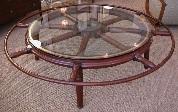 A gallant and massive English chestnut and brass ship's wheel now mounted as a table with glass top; the large-scaled wheel composed of 8 turned spokes centered around an iron hub; the inner ring with brass inlay; raised on later supports