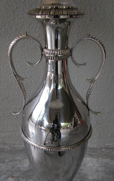 A sleek American art deco nickel-plated double-handled urn now mounted as a lamp; with slender flared neck flanked by graceful handles; above an elongated bulbous body over a splayed base with floral vine relief.