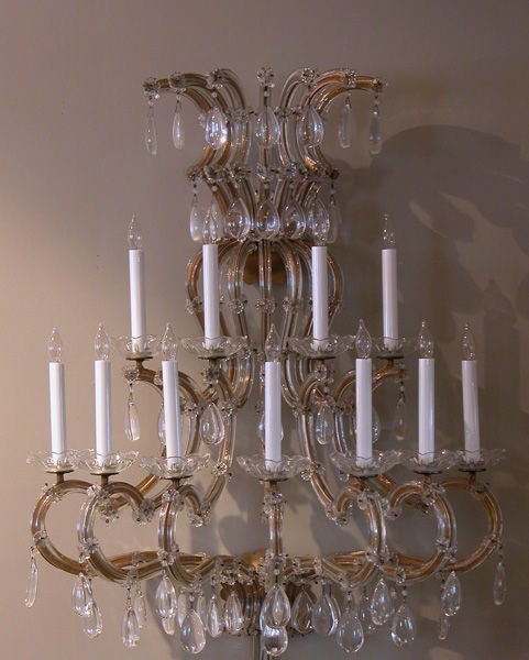 A monumental and voluptuous pair of French Maria Theresa style 1950's 2-tier 11-arm wall sconces; each of impressive graduated size composed of a curvaceous gilt-metal frame sheathed in clear glass adorned with crystal pendants
