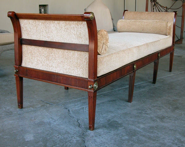 An elegant French Louis XVI mahogany bench or daybed; the long rectangular loose cushion seat flanked by padded outscrolled ends; above a fluted apron all over 8 fluted quadrangular supports