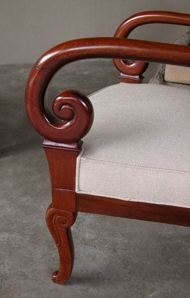 A richly-colored and gracefully proportioned pair of French Restoration period mahogany armchairs; each with arching crest rail above dramatically scrolled arms above lotus leaf carving; the bowed seat with plain frieze apron raised on console legs