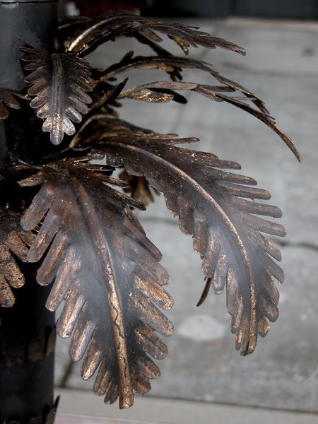 A whimsical pair of French 1940's ebonized-tole palm tree form lamps with gilded highlights; each tall lamp of ebonized tole surmounted by a lively crown of downscrolled leaves raised on an imbricated stem all above an octagonal base