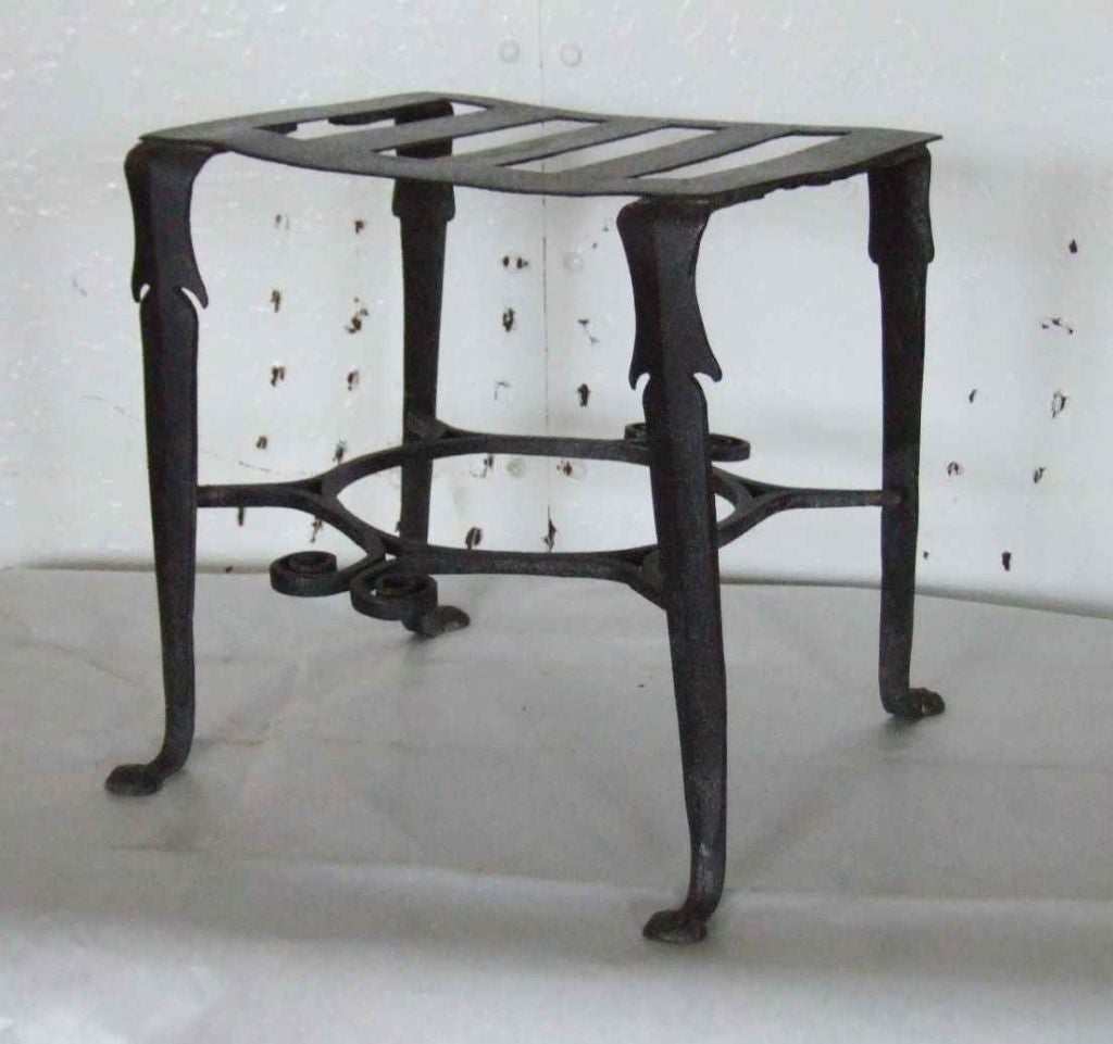 English 18th century wrought iron trivet, the slatted top over unusual shaped legs ending in penny feet, joined by wrought stretcher having scrolled front and back.