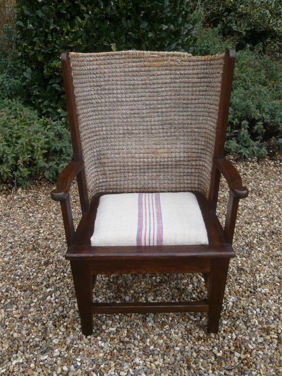 An English Orkney chair of traditional form with barrel back of hand woven hemp to protect the sitter from drafts, and cushion seat on wooden frame with arm supports and box stretcher.