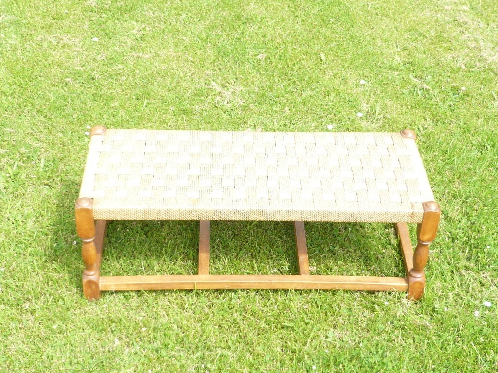 An English 1920's oak stool with box and cross stretchers and a woven rope top, often used for luggage at the foot of a bed.