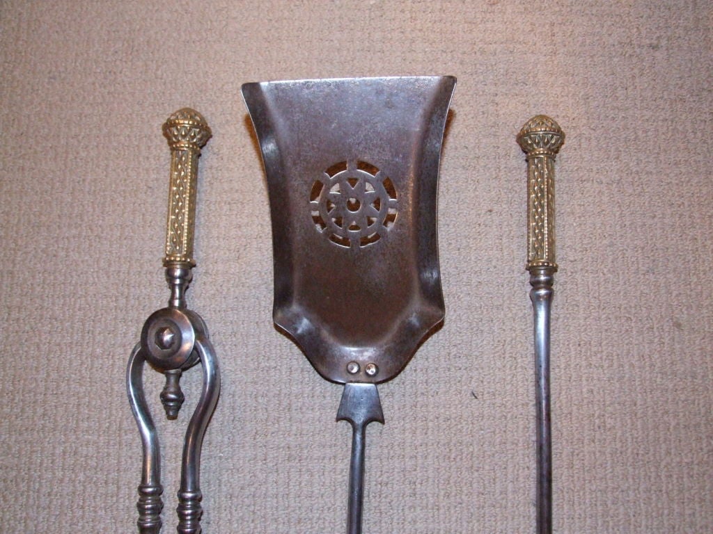 A fine set of three Regency period English firetools comprising poker, tongs and shovel, in gunmetal steel with decorative bronze handles and round cut-out piercework on flared shovel bowl.