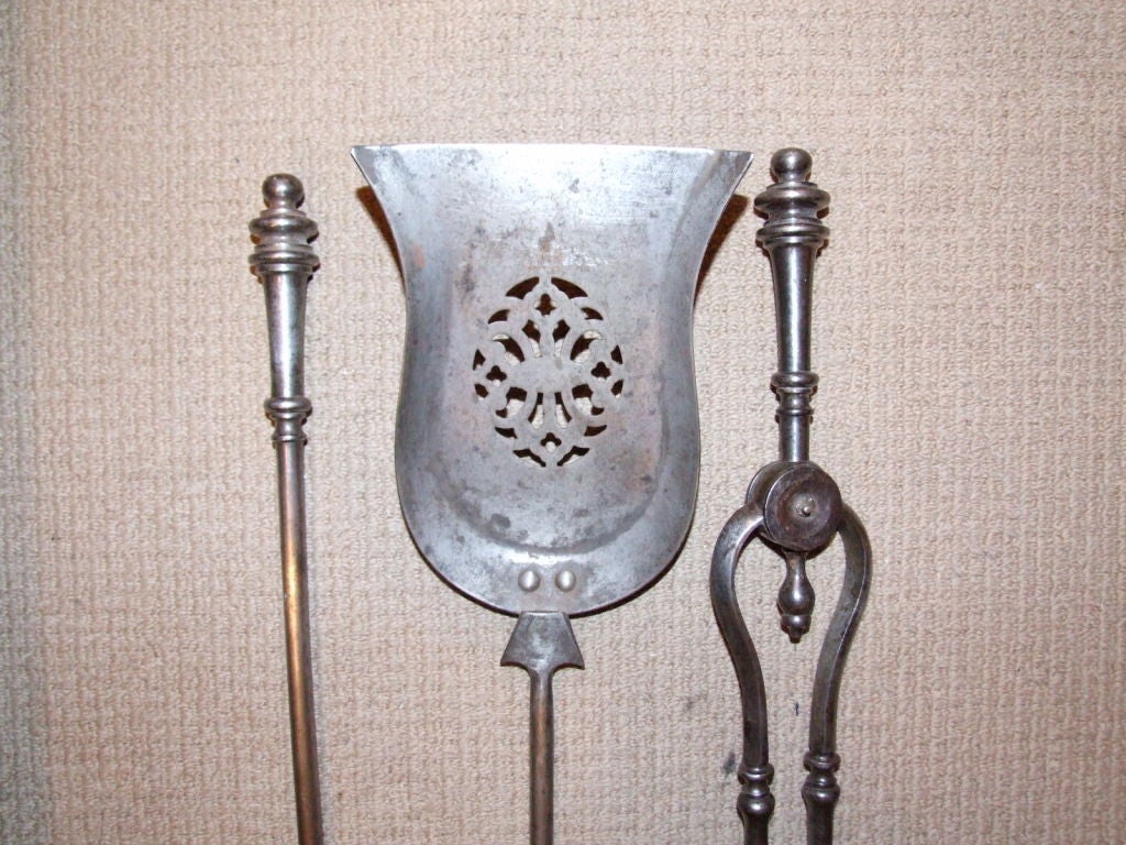 A set of three Regency period English firetools comprising poker, tongs and shovel, in gunmetal steel double button finials and oval cut-out piercework on shaped shovel bowl.