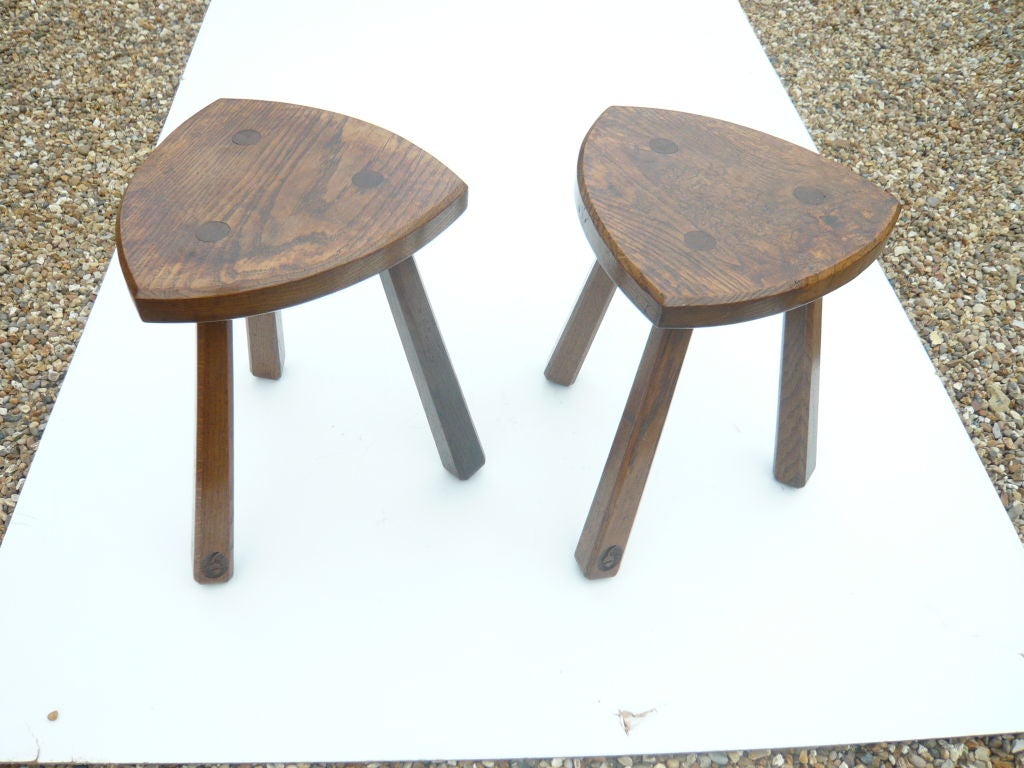 A pair of well crafted early 20th century English elm stools having rounded triangular tops on three turned legs, with each stool having acorn motif carved in one leg.  Beautiful color and graining
