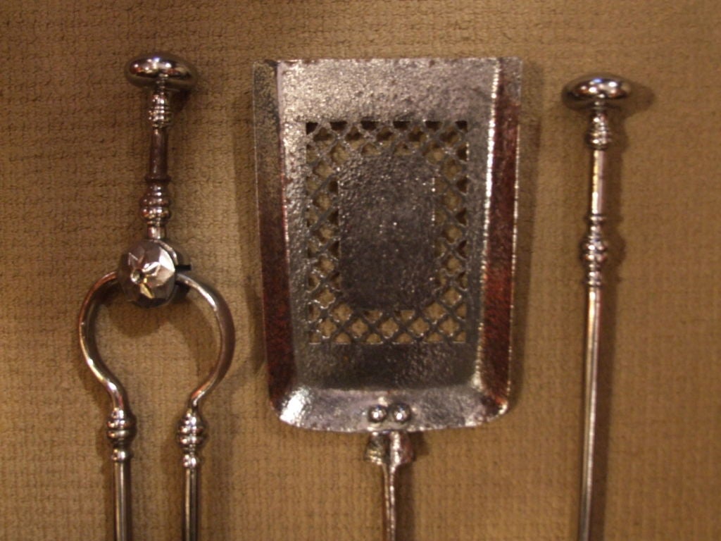 A set of three Regency period English firetools comprising poker, tongs and shovel, in polished gunmetal steel large flat button finials and geometric cut-out piercework on square shovel bowl.