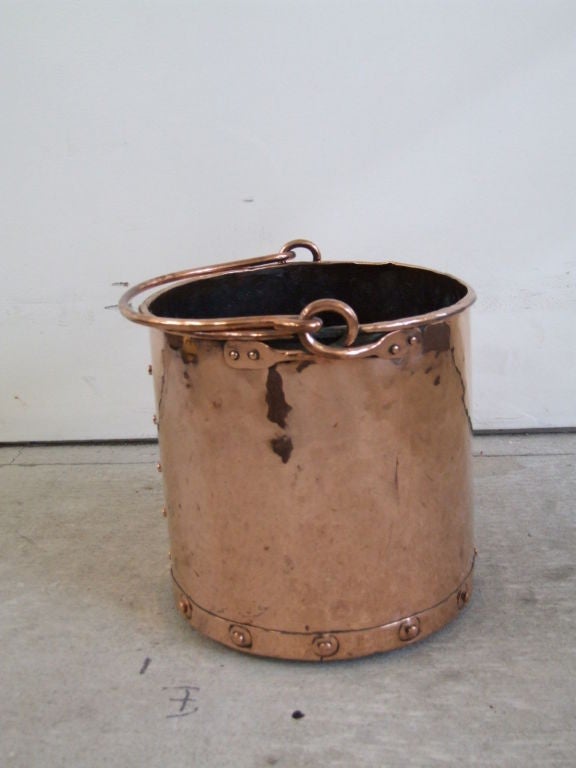 A 19th century English brass bucket with rivetted seams having overturned lip and brass handle with looped and rivetted handle supports.  Useful next to a fireplace for kindling, or as a handsome waste bin.

firewood, kindling, log holder