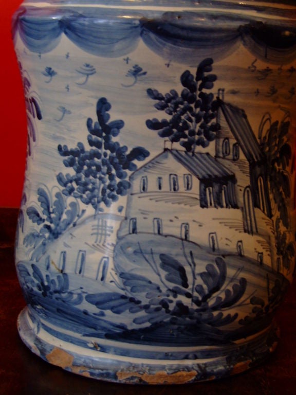 An 18th century Italian apothecary jar with blue and white tin glazing and hand painted decoration depicting a hilltop village in a lush setting.  Attractive shape and rare size.